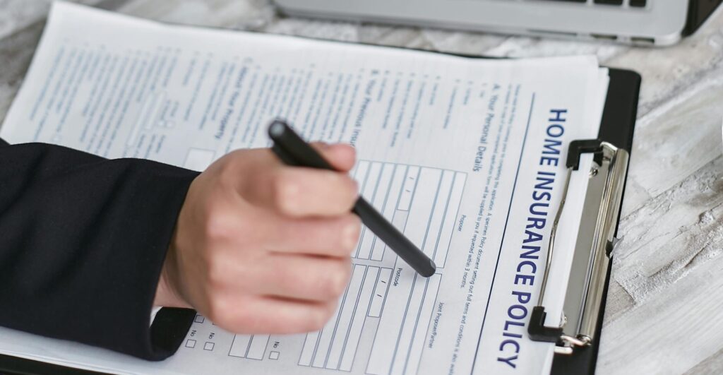 pexels-photo-7734611-7734611 An adult reviews and signs a home insurance policy document on a clipboard next to a laptop.